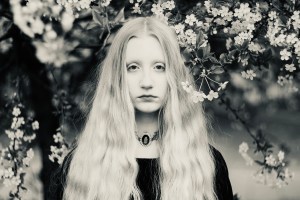 Woman with blonde hair standing near green leaf tree