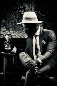 Man in gray suit and brown hat sitting on brown wooden bench