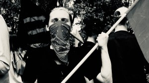 masked person holding a flag in front at a crowd at a protest